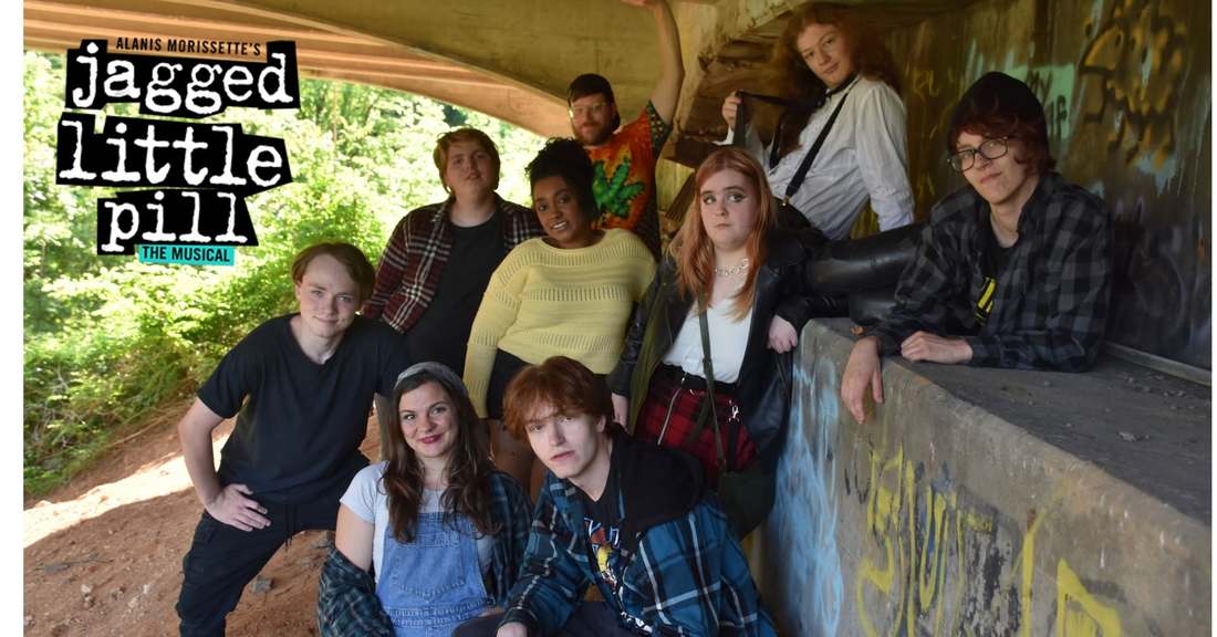 Jagged Little Pill cast members in costume posing together beneath a bridge