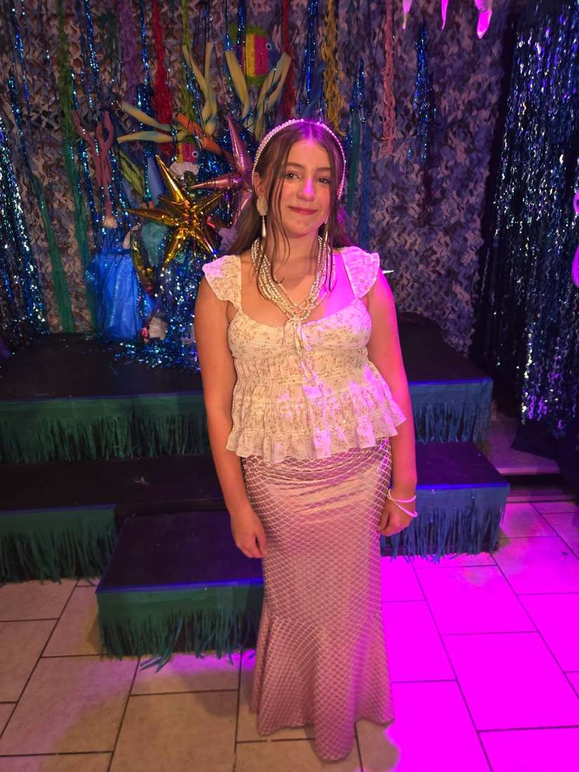 A mermaid sister in a light pearl dress with layered pearl necklaces