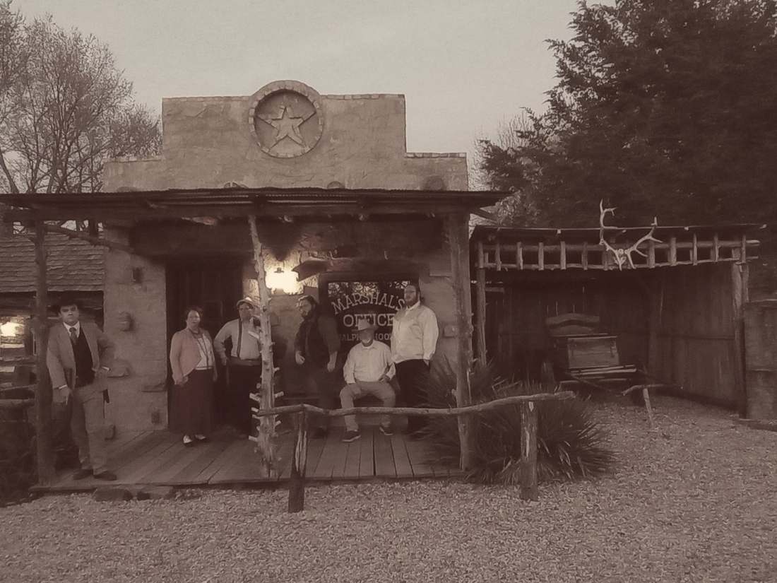 Cast members gathered on the porch of an old marshal's office (sepia)