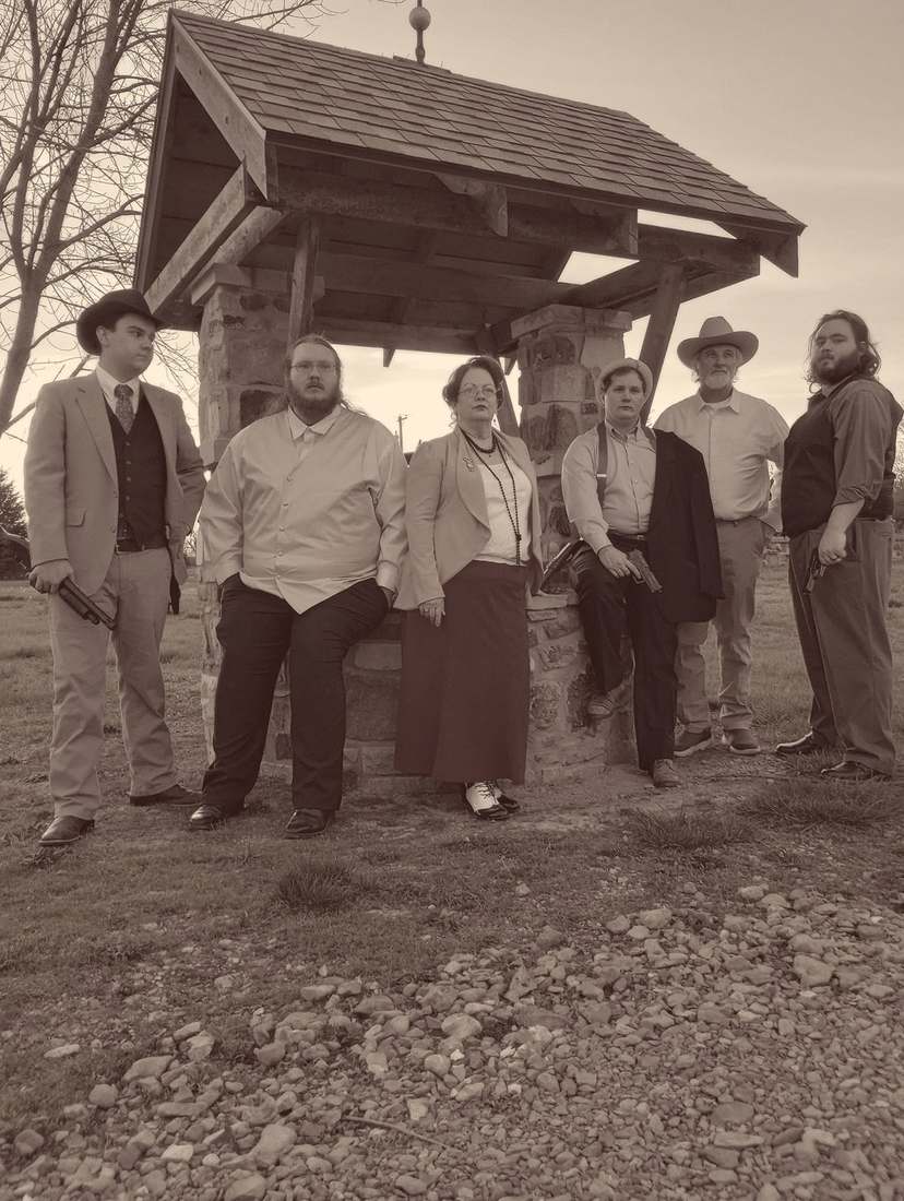 Six cast members posing beneath a stone wishing well (sepia)