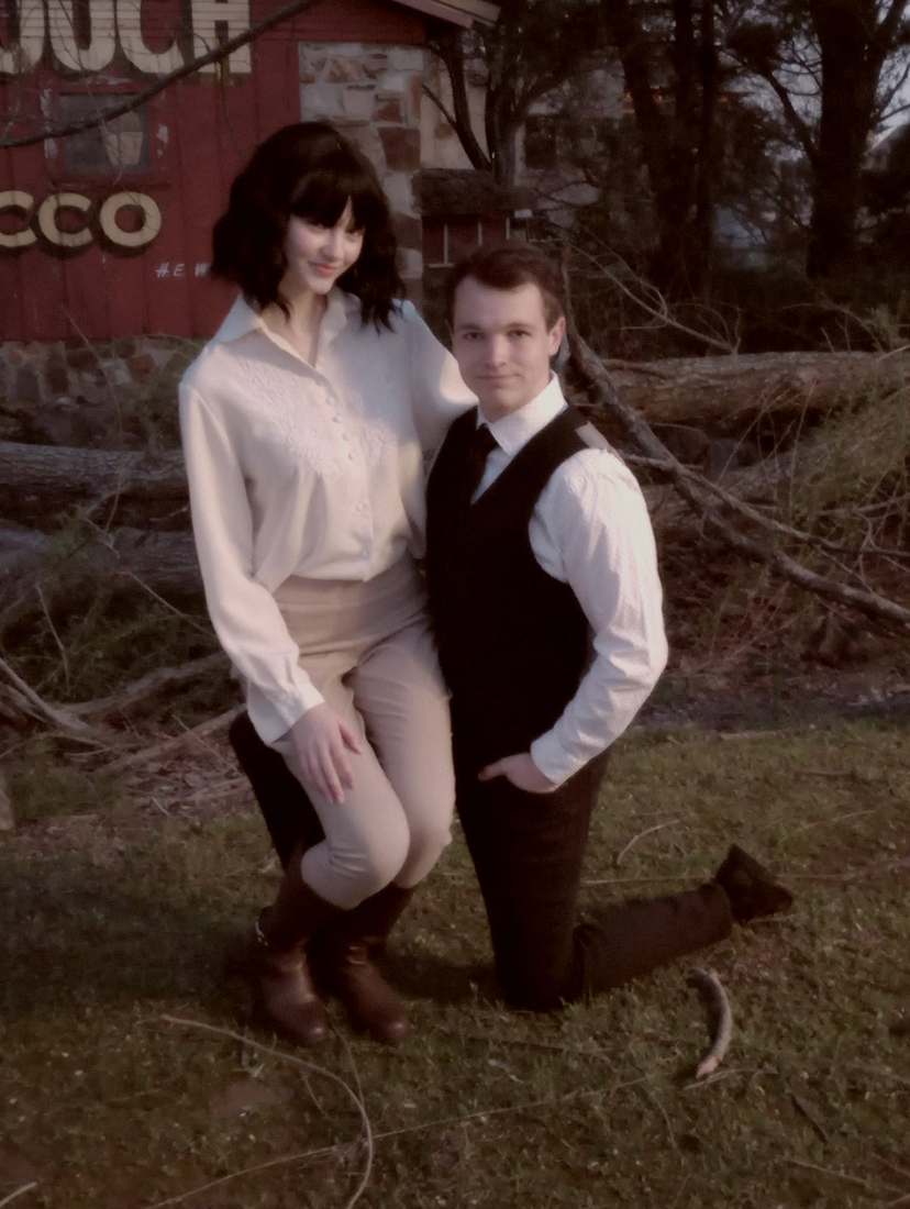 Two cast members posing by a fallen log in front of a red barn