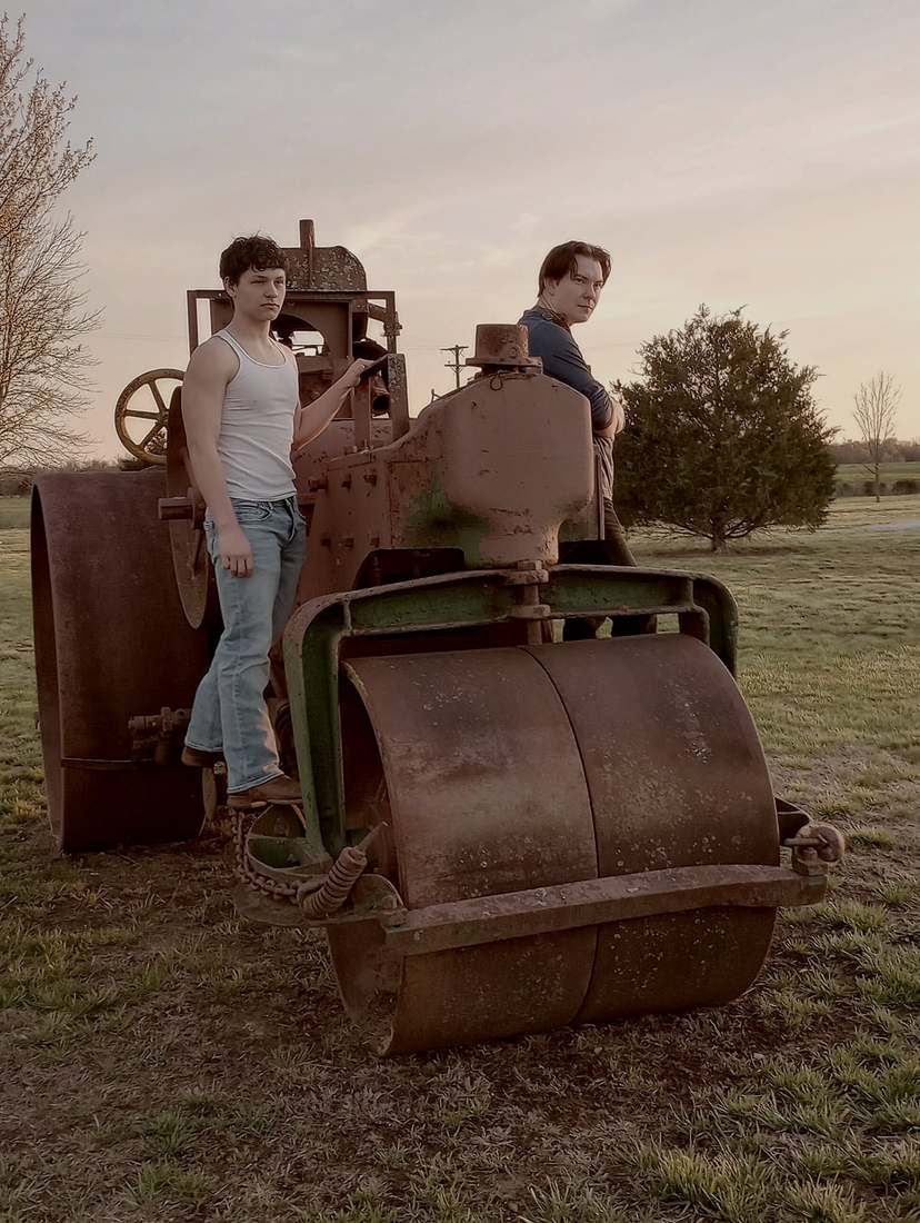Two cast members posing on a vintage steamroller at sunset