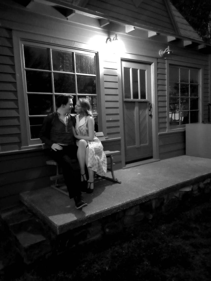 Bonnie and Clyde sitting close on a porch bench under a lamp at night (black and white)