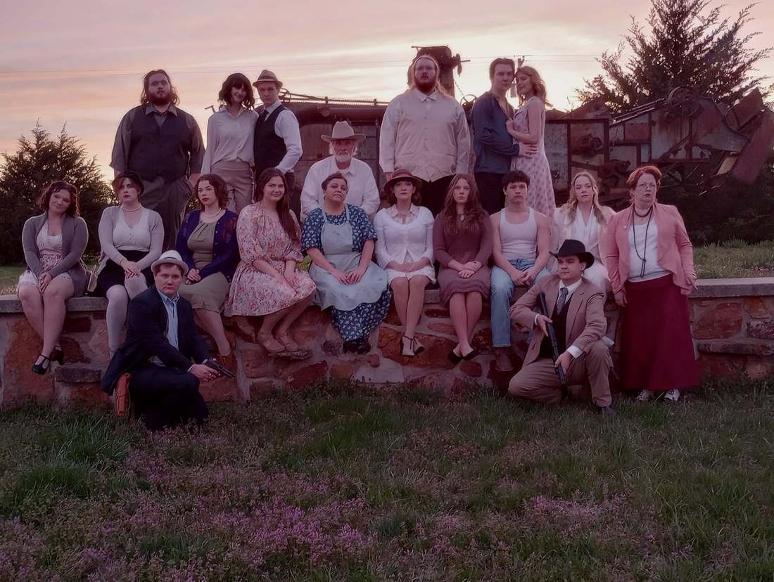 The full Bonnie & Clyde company posed on a stone wall at sunset