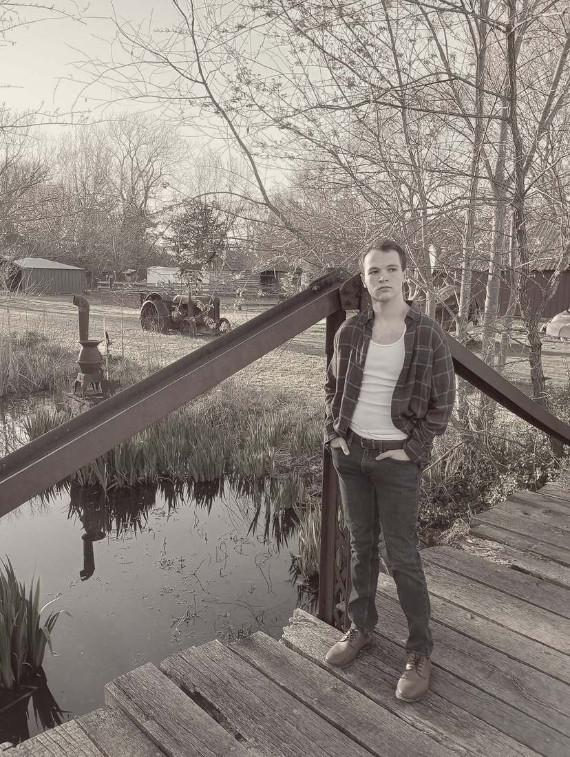 Clyde standing on a wooden footbridge over a pond, a vintage tractor behind him (sepia)