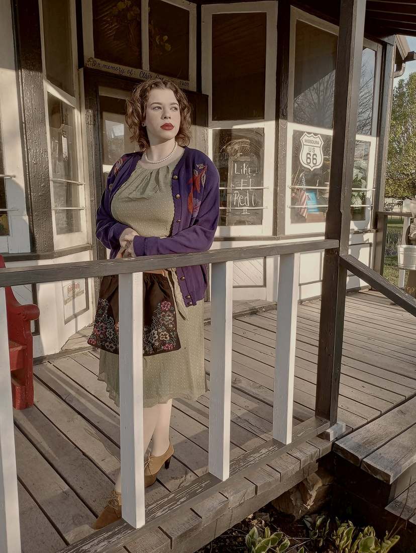 Bonnie leaning on the rail of an old store porch, a Route 66 sign in the window