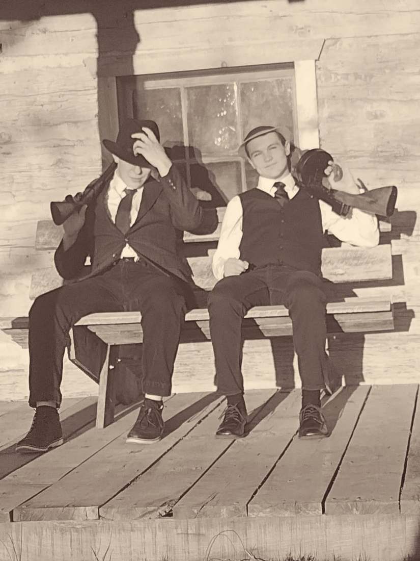 Two cast members with Tommy guns sitting on a cabin porch bench (sepia)
