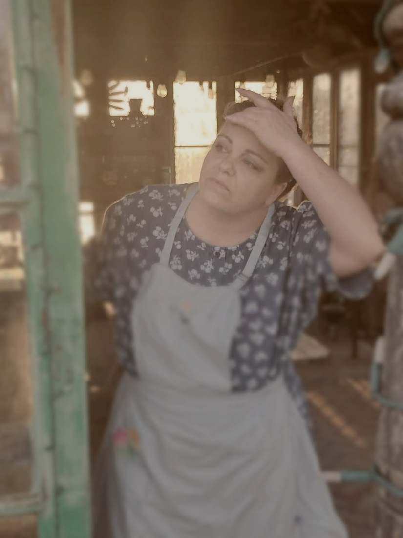 A cast member in a floral dress and apron shielding her eyes from the sun in a doorway