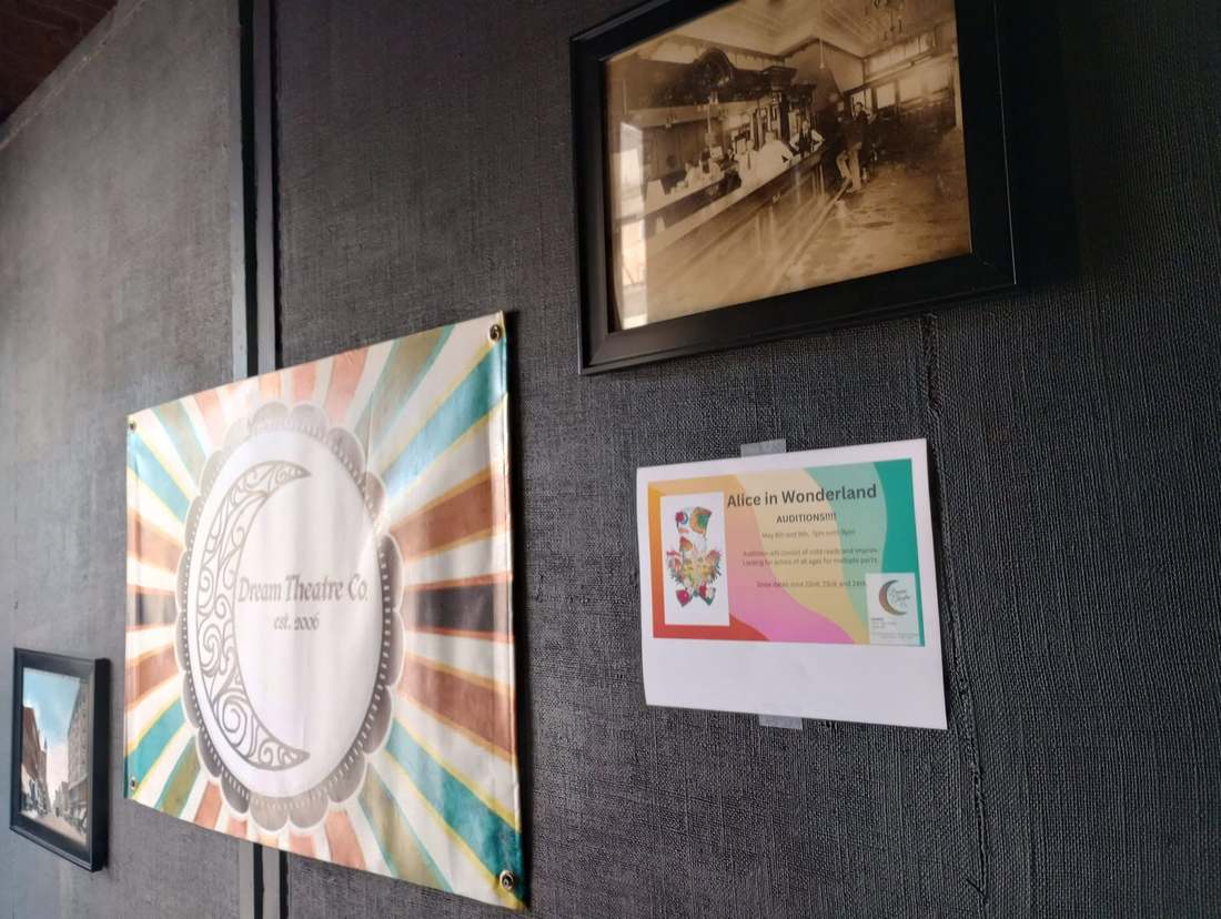 The studio wall with the Dream Theatre Co. banner, a framed vintage saloon photo, and an audition poster