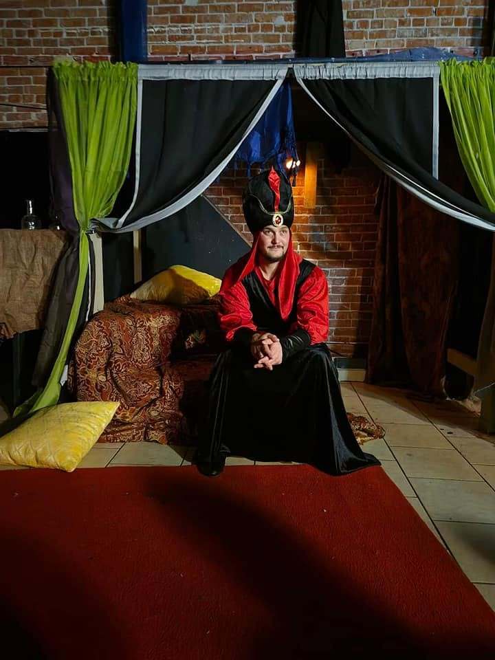 The Royal Vizier sits alone on the palace couch, hands folded, in Twisted