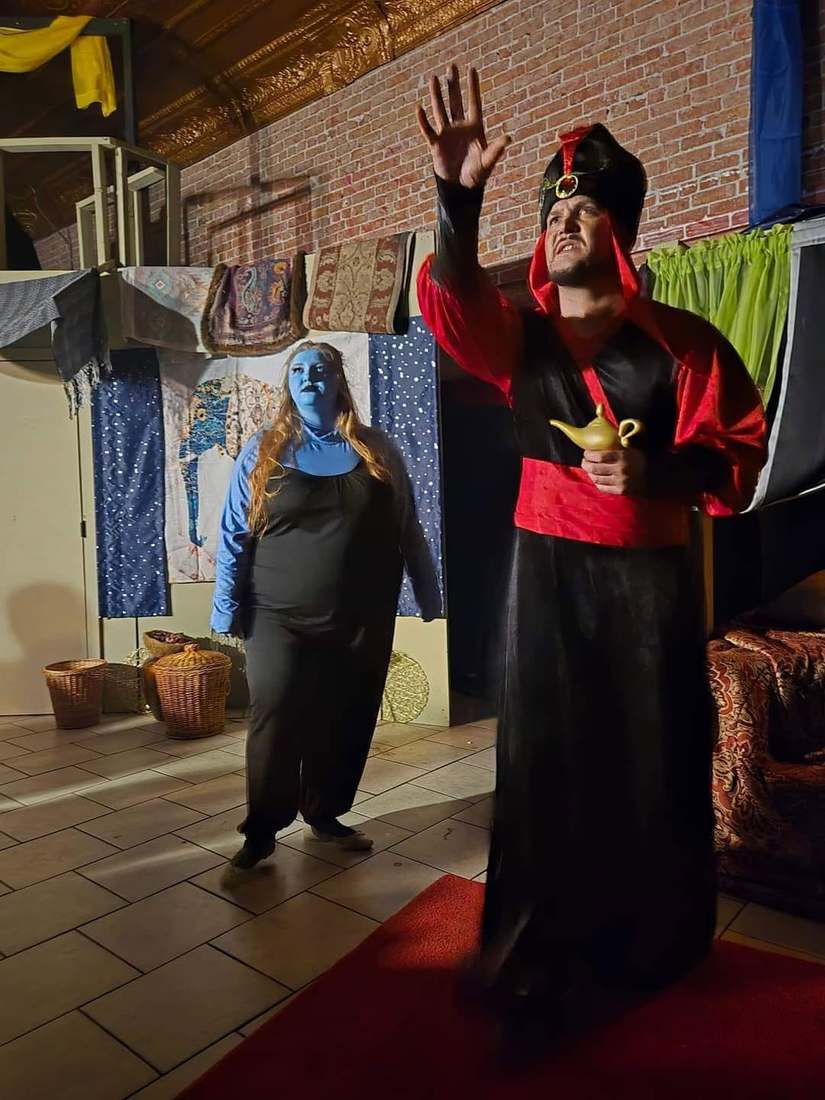 The Vizier raises a hand in triumph, lamp in the other, the Djinn behind him