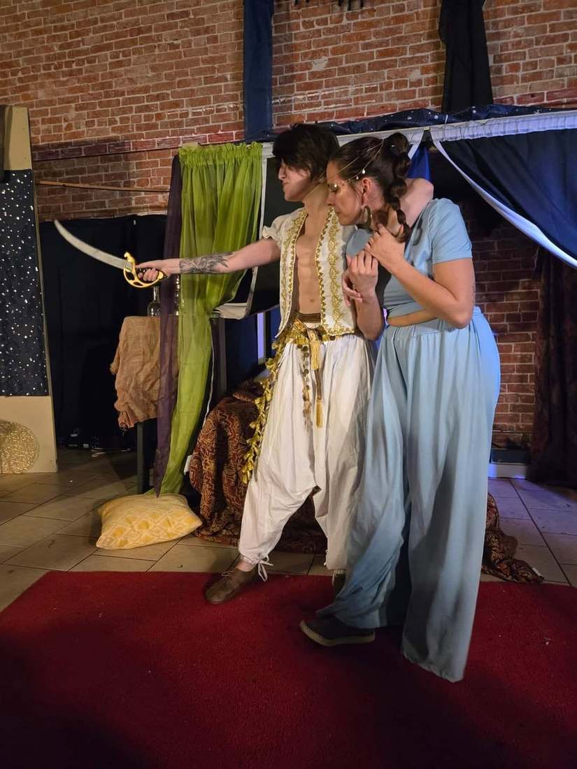 The prince levels his scimitar as he shields the princess in Twisted