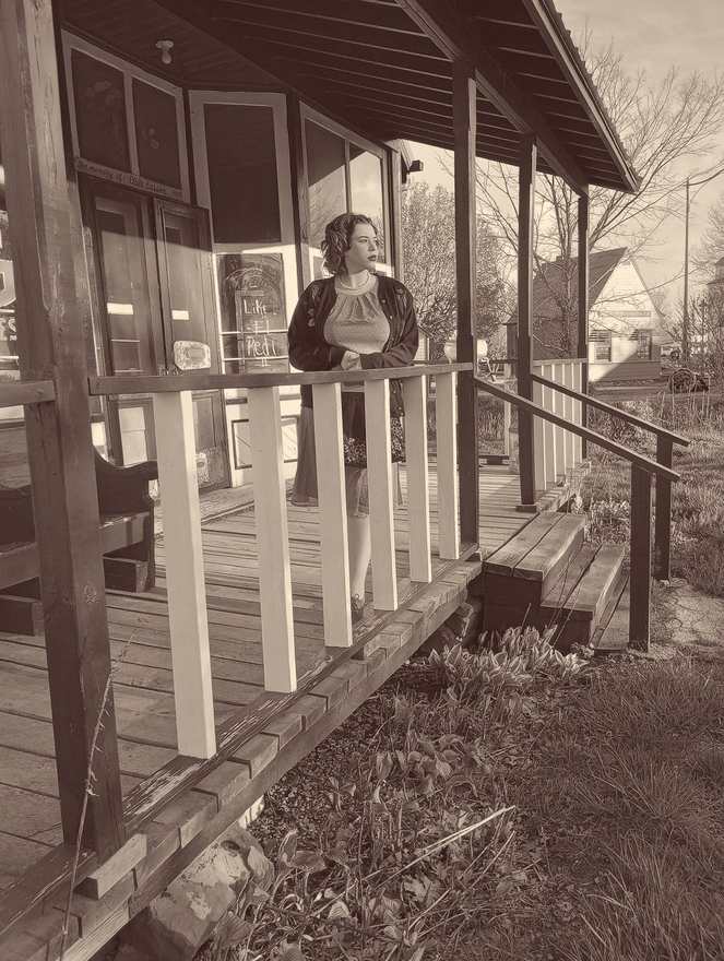Bonnie leaning on the rail of the old store porch (sepia)