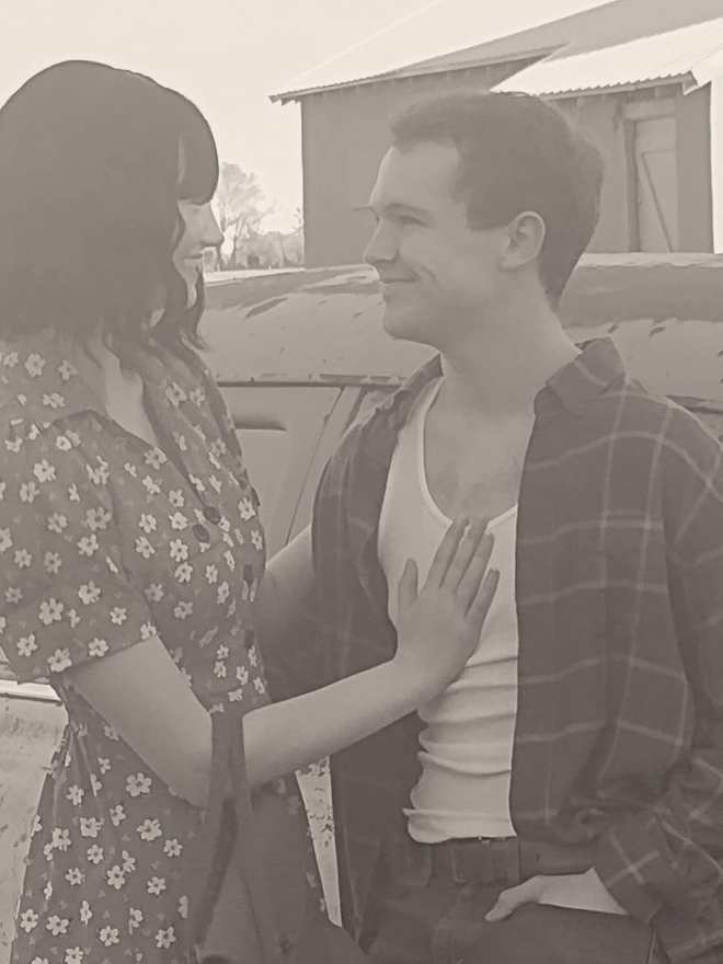 Bonnie and Clyde smiling at each other beside the vintage car, close up (sepia)