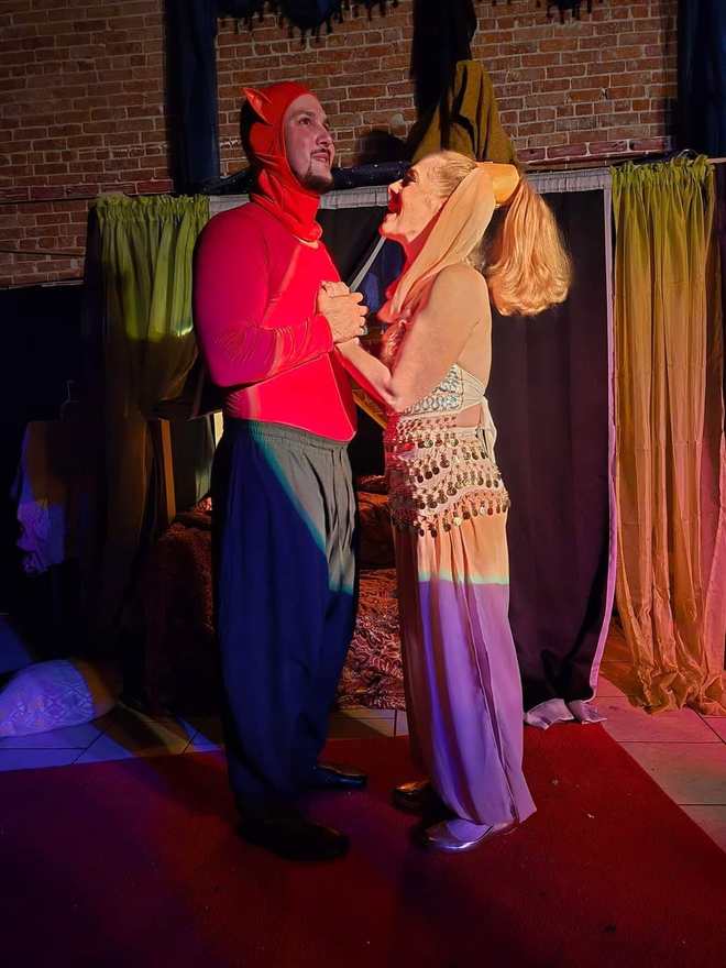 A smiling pair clasps hands mid-scene — he in red, she in a coin-belt costume