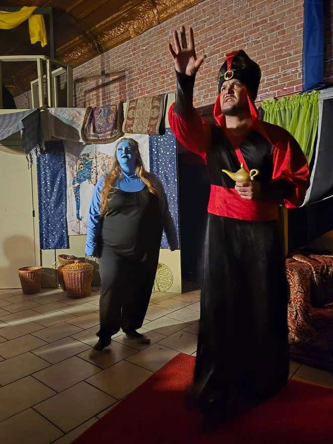 The Vizier raises a hand in triumph, lamp in the other, the Djinn behind him