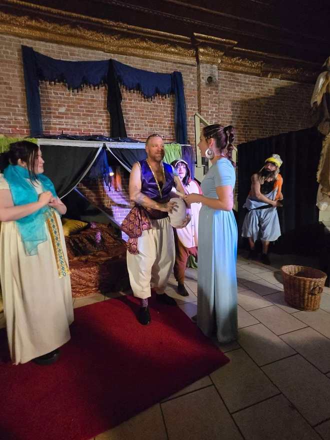 The prince and princess talk in the marketplace, a basket at their feet