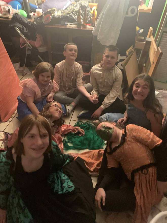 The young cast grins at the camera from their backstage circle