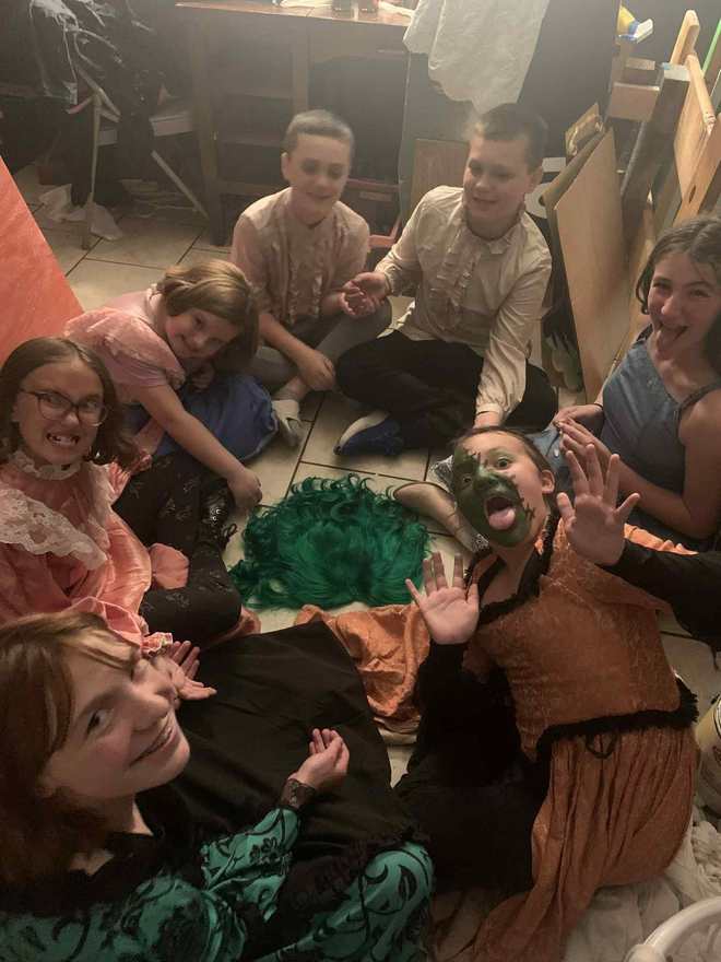 Cast members pull silly faces backstage, the creature waving at the camera in green makeup