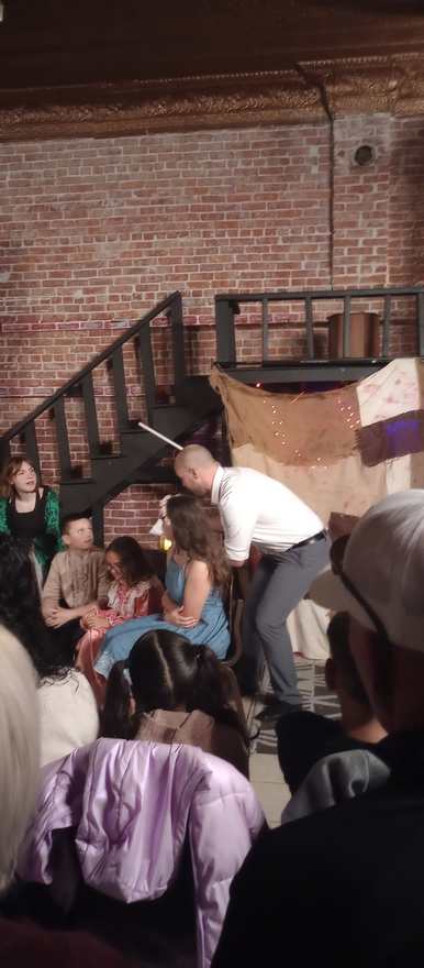 A performer leans in close to the seated young cast during a Frankenstein scene