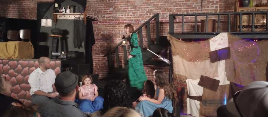 A performer in a long green dress carries a lantern down the stage stairs