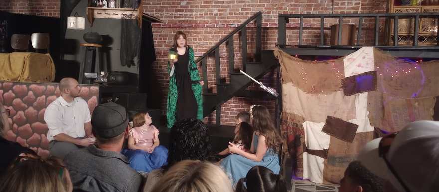 The performer in green addresses the seated cast, lantern in hand
