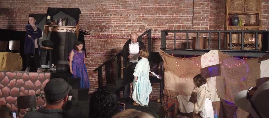 A young performer in a pale nightgown faces the company on stage