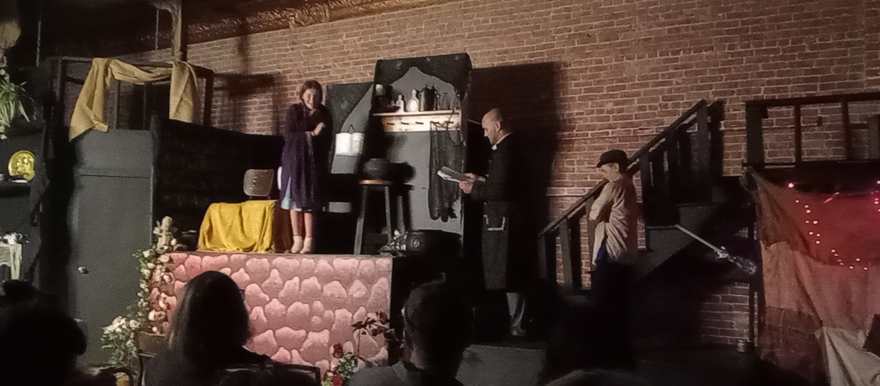 Three performers play a scene across the raised stone platform and stairs