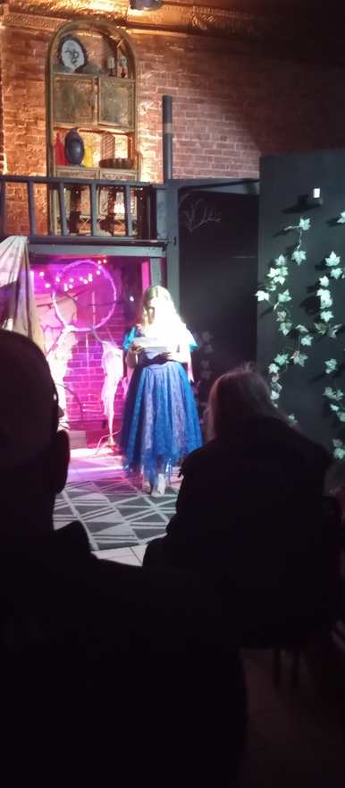 A performer in a blue gown reads beneath the pink-lit circular archway