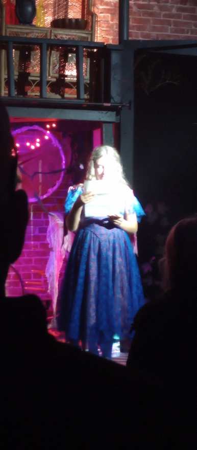 A close view of the performer in blue reading from her pages in pink light
