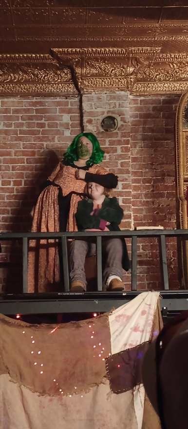The green-wigged creature embraces a young performer on the balcony