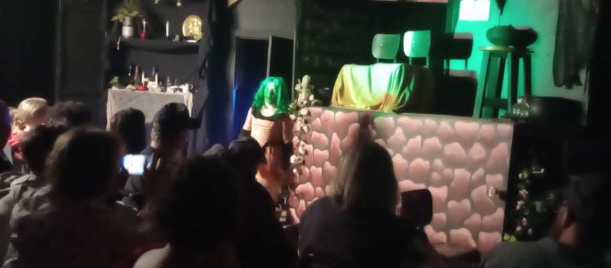 The creature approaches the draped platform under green light