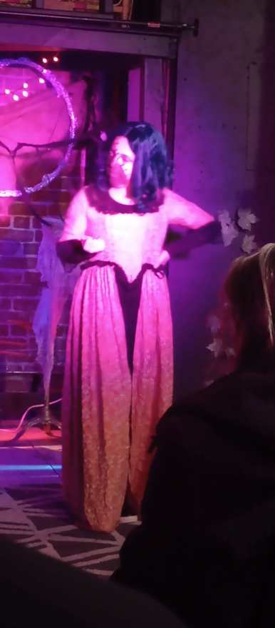 A close view of the performer in the pink dress, hands on hips in purple light