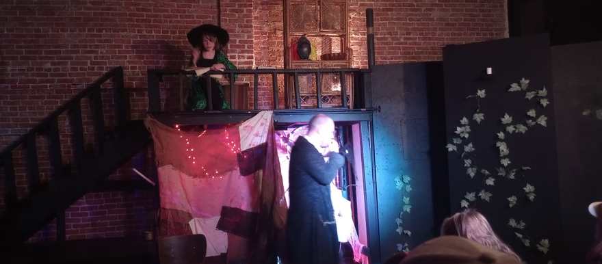 The hatted performer watches from the balcony over a scene below