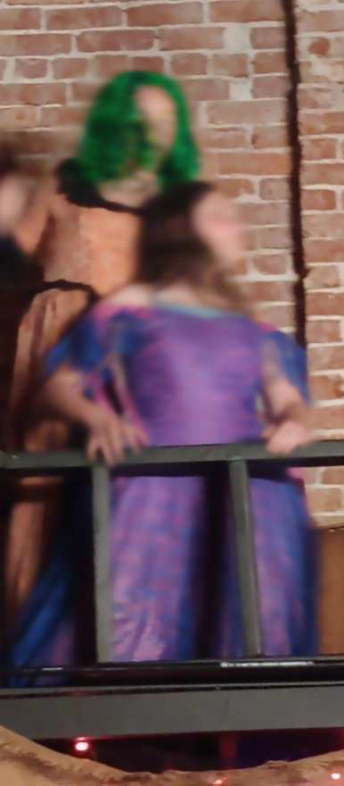 The performer in purple leans on the balcony railing beside the creature