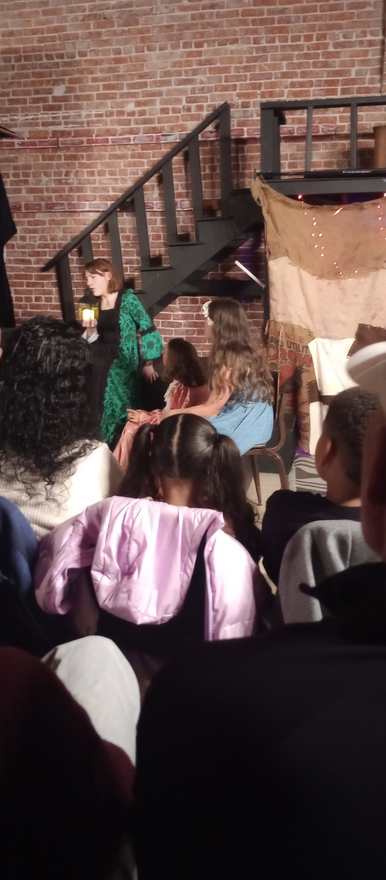 The performer in green returns with her lantern to the seated cast