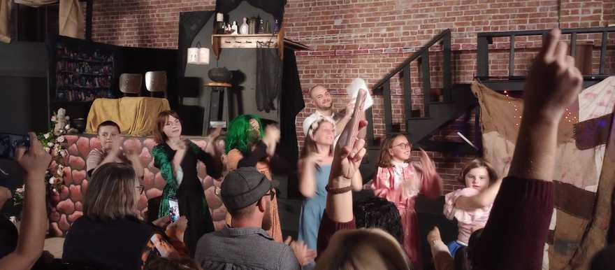 The cast cheers and waves at the curtain call as the audience applauds