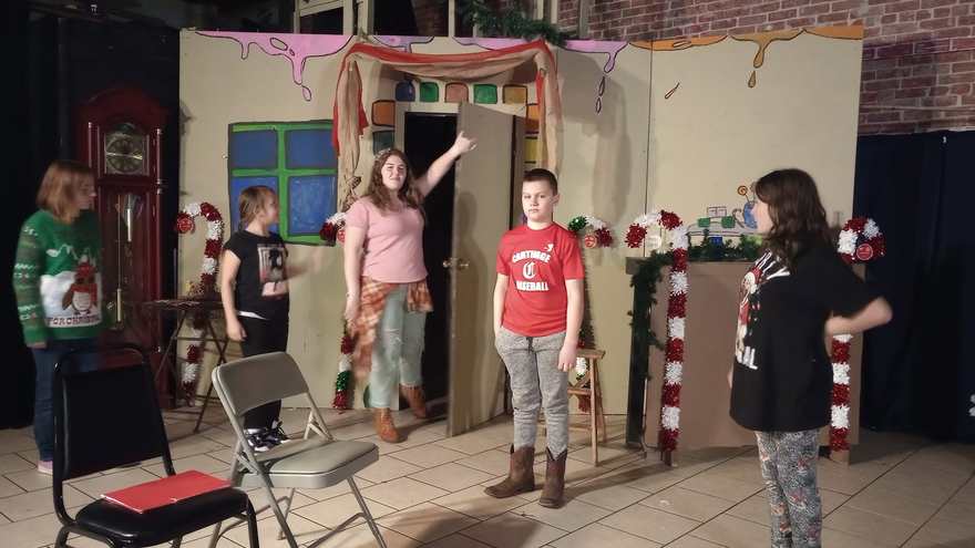 A performer in pink raises her arm in the doorway flat as her castmates look on