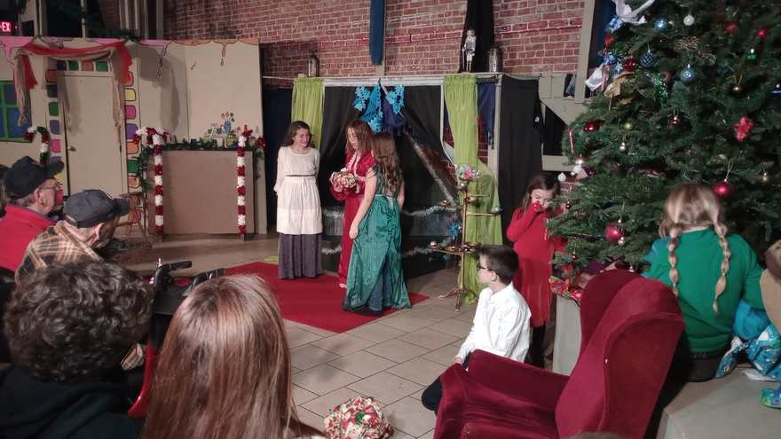 Two performers in long gowns — one in white and red, one in teal — face each other on the red carpet