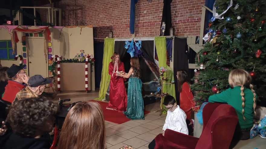 The performers in red and teal gowns hold hands center stage as the audience watches