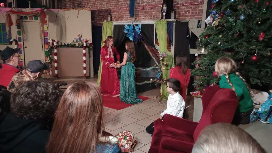 The gowned pair play their scene before the children seated around the red carpet