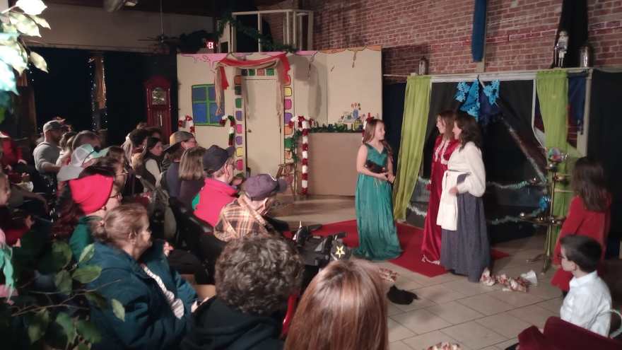 Performers in gowns gather at the side of the stage as the audience looks on