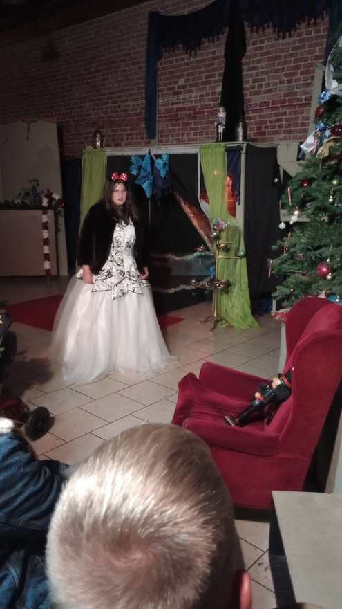 A performer in an elaborate white gown with a dark bodice stands center stage