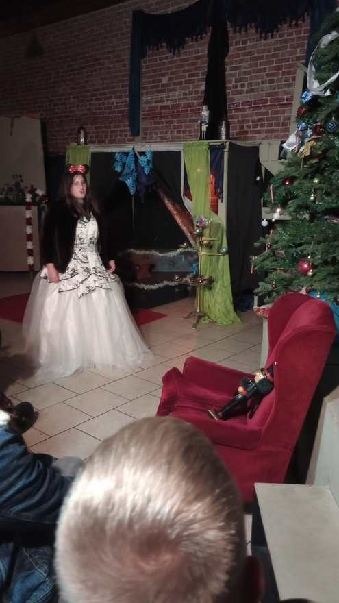 The performer in the white gown poses center stage, the Christmas tree and draped set behind her