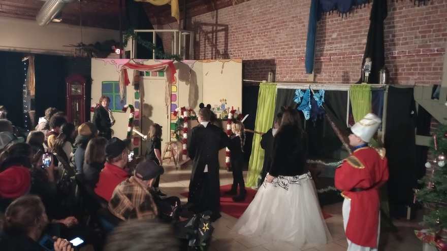 The full stage in performance — cast, Christmas tree, and the audience ringing the red carpet