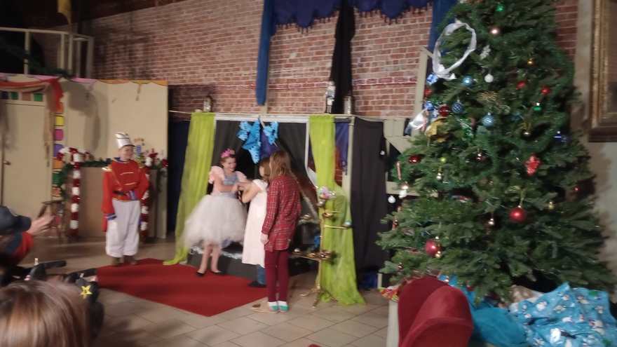 Clara, the Nutcracker, and a castmate in red gather by the decorated Christmas tree