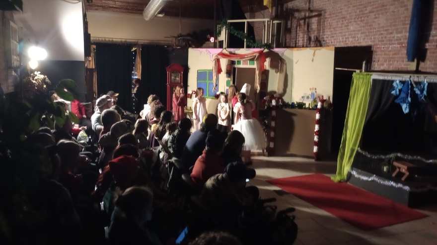 A wide view of the darkened studio, the audience watching the lit stage at the far end
