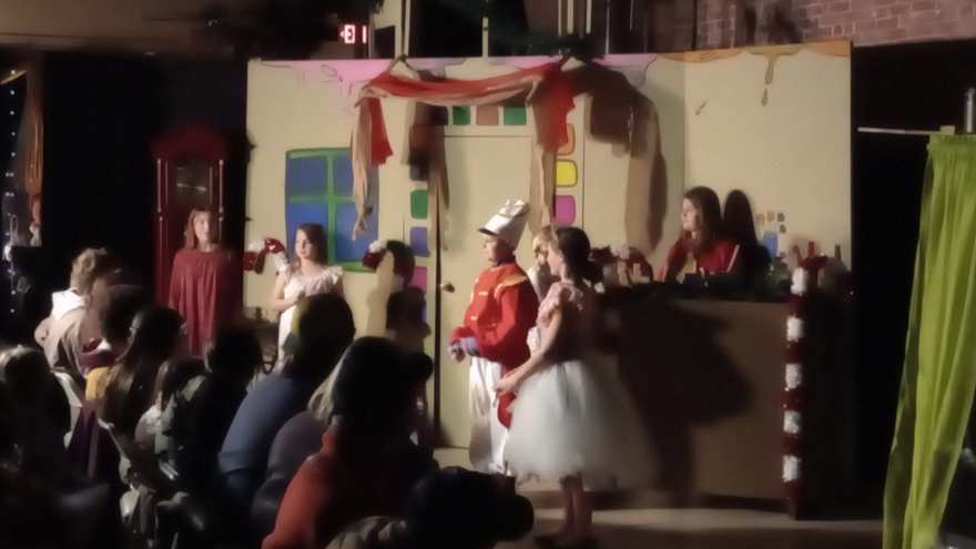 The Nutcracker and Clara stand at the candy counter flat as cast members watch from behind it