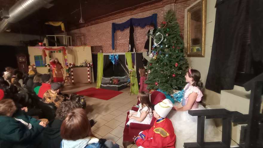 From the side of the house, children in costume sit on the sofa and watch the scene at the far end