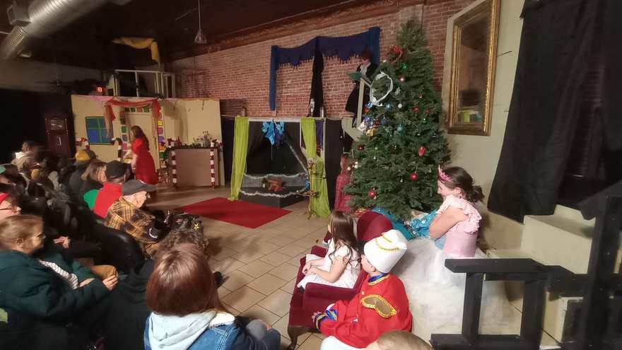 A side view of the performance, the young cast seated along the sofa as the scene unfolds